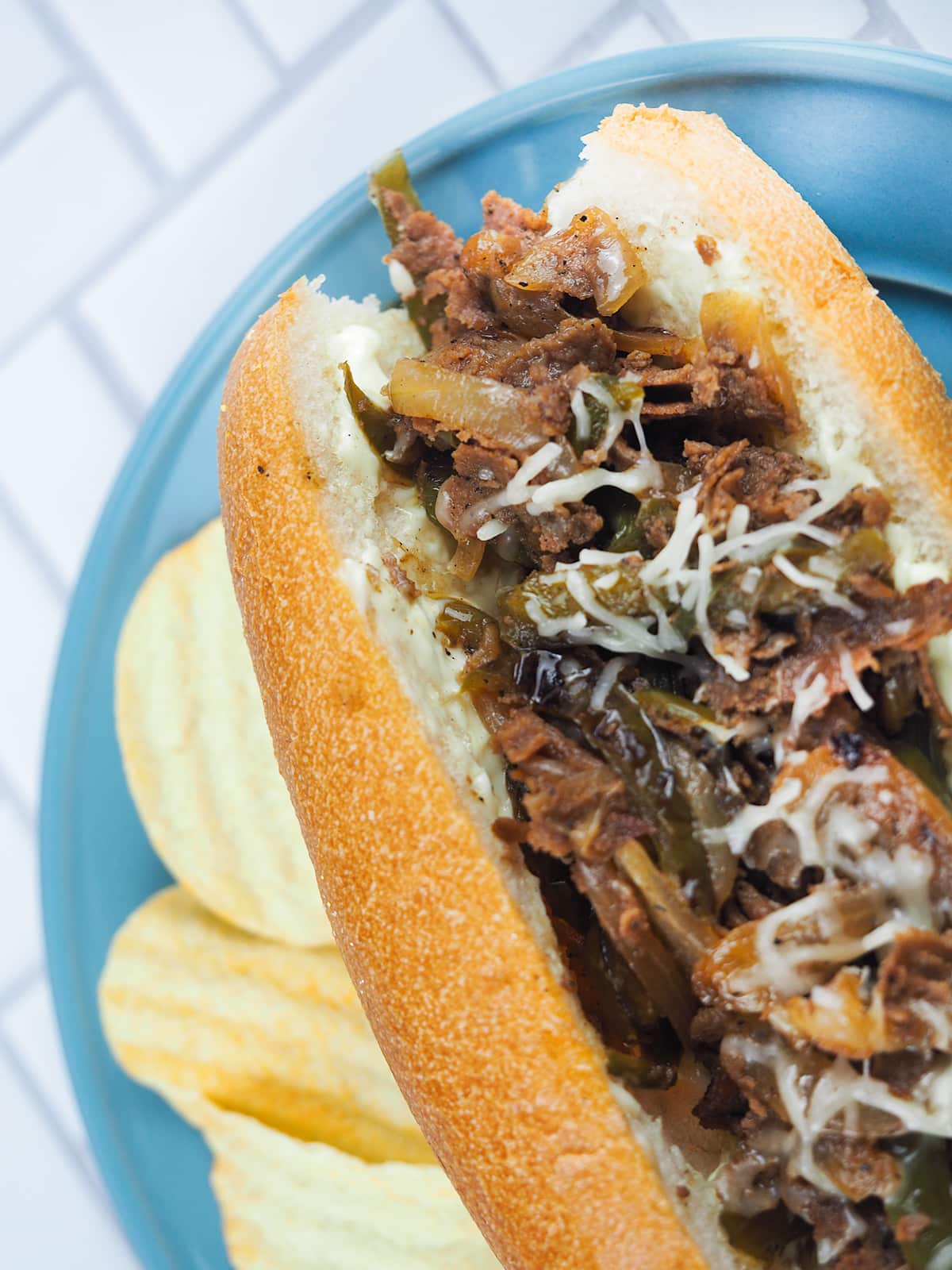 philly cheesesteak on blue plate with chips
