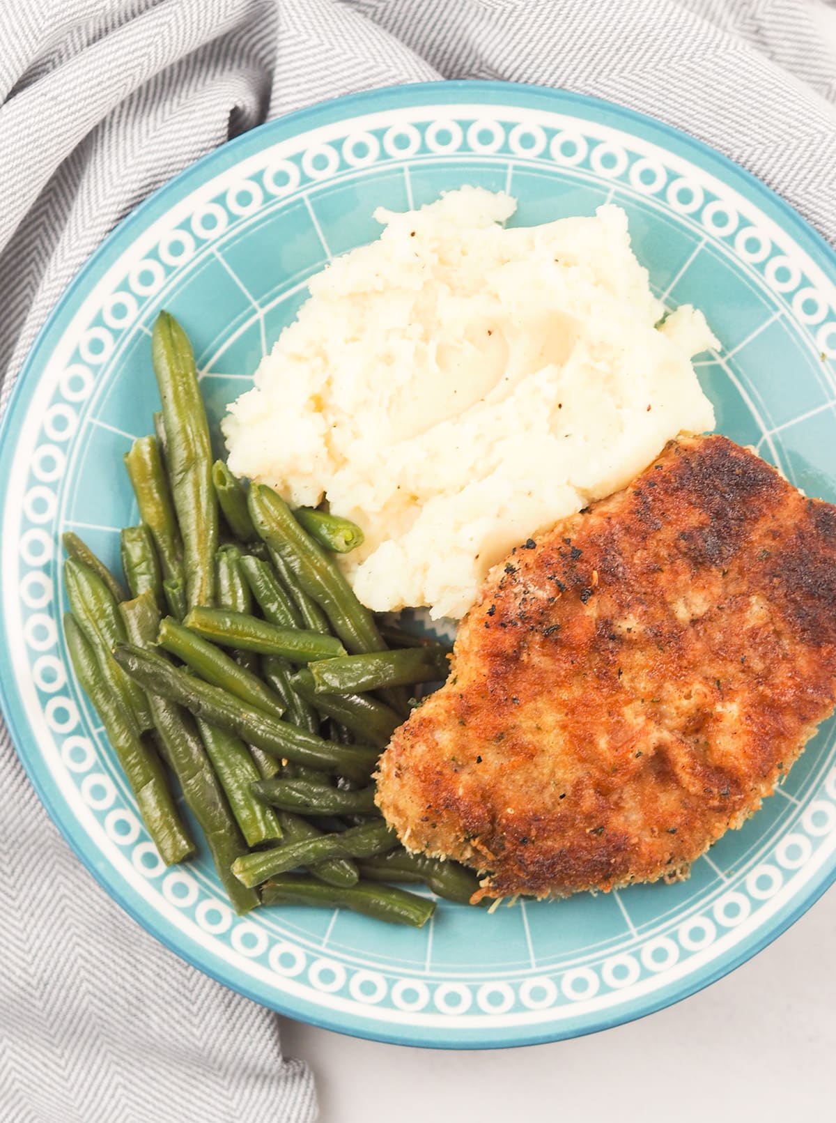 breaded pork chop on blue plate with green beans and mashed potatoes