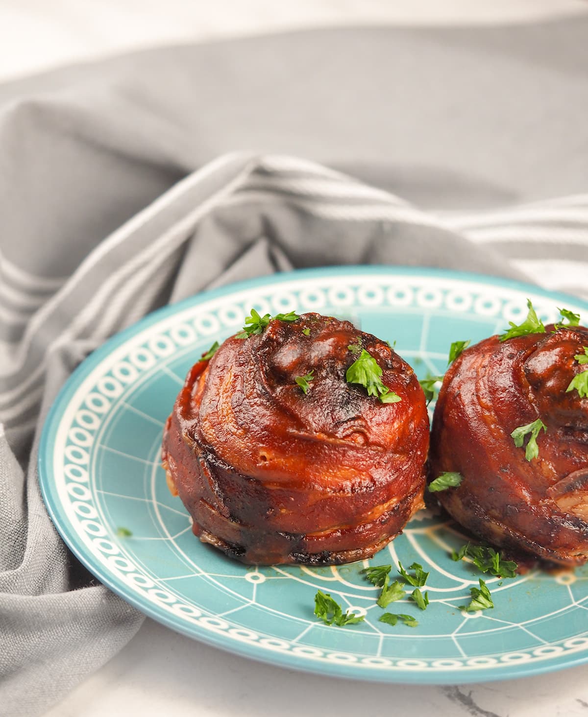 bacon wrapped onion bombs on blue plate next to grey striped linen towel