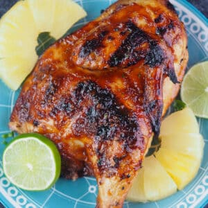 grilled half chicken on plate with pineapple and limes