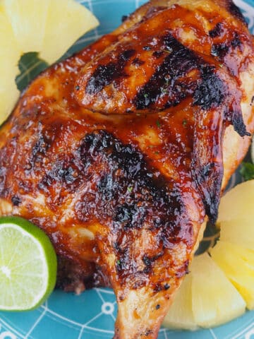 grilled half chicken on plate with pineapple and limes