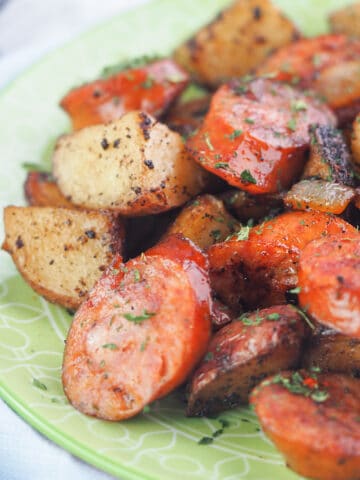 Close view of sliced smoked sausage with fried potatoes on a green plate.