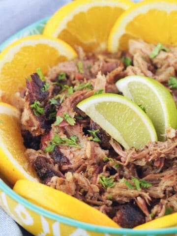 Close view of shredded mojo pork in yellow bowl with green rim with slices of citrus.