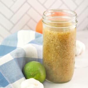 mojo marinade in jar sitting next to citrus and garlic