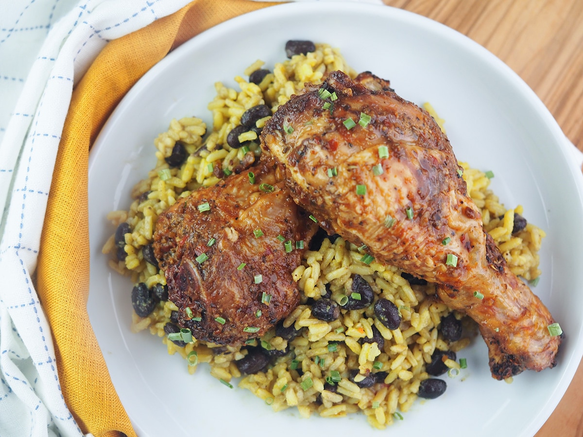 Grilled BBQ chicken legs on a bed of yellow rice and beans.